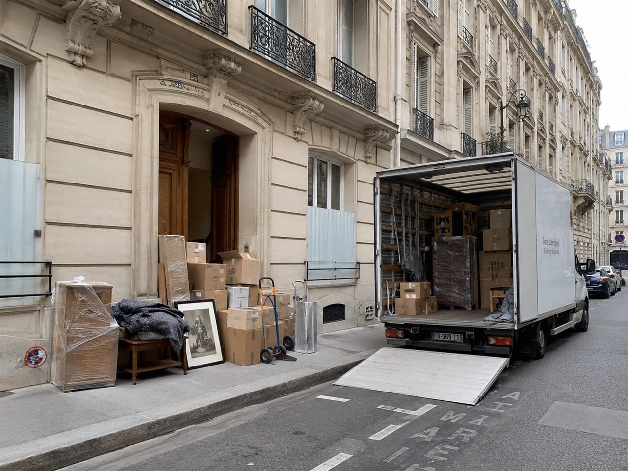 Camion de débarras chargé devant un immeuble parisien, avec cartons et mobilier